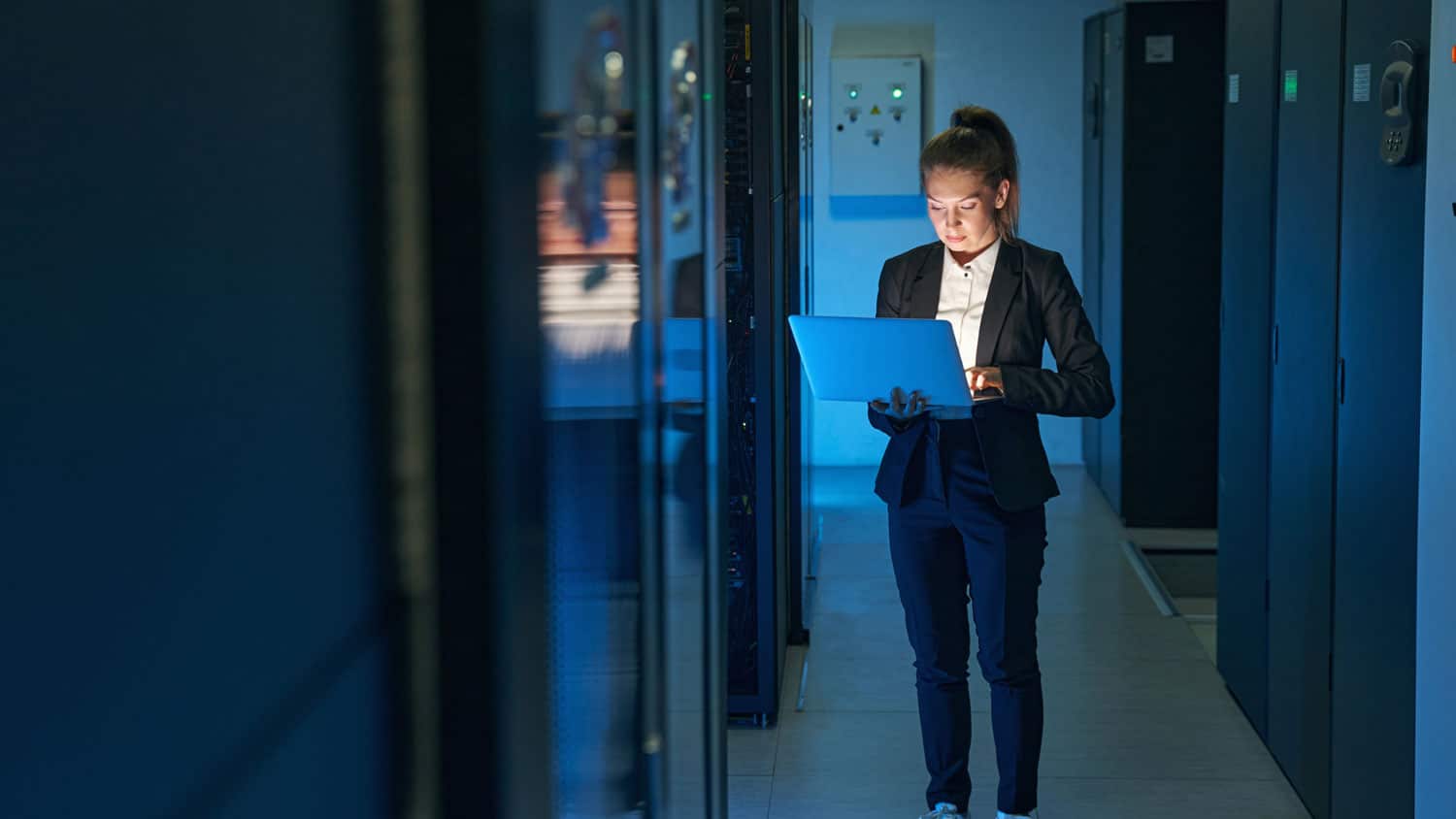 woman holding computer by data servers in a data center